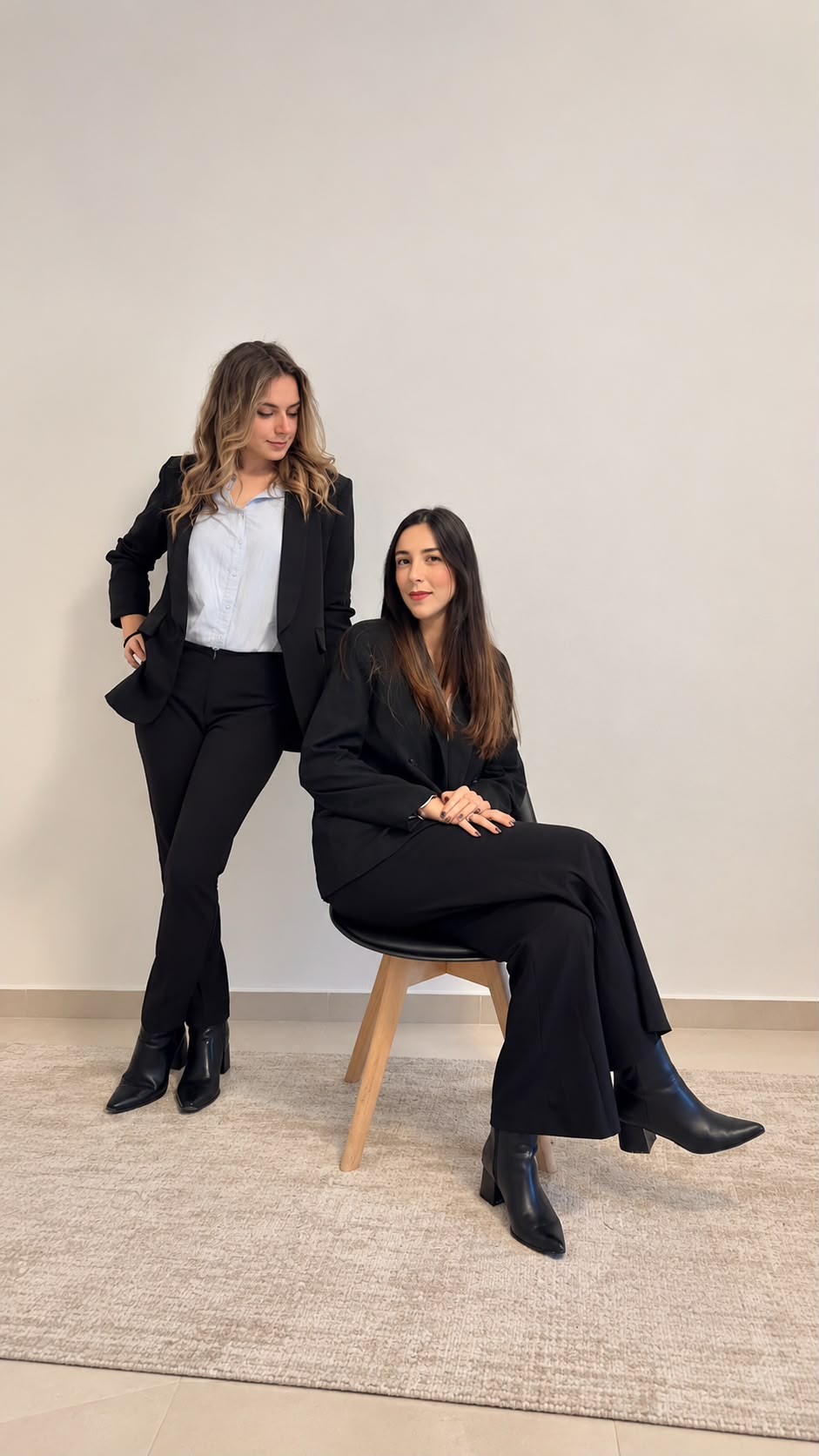 Alessandra Ajdini in piedi e Martina Bianchini seduta su uno sgabello, entrambe in tailleur nero, davanti a una parete chiara